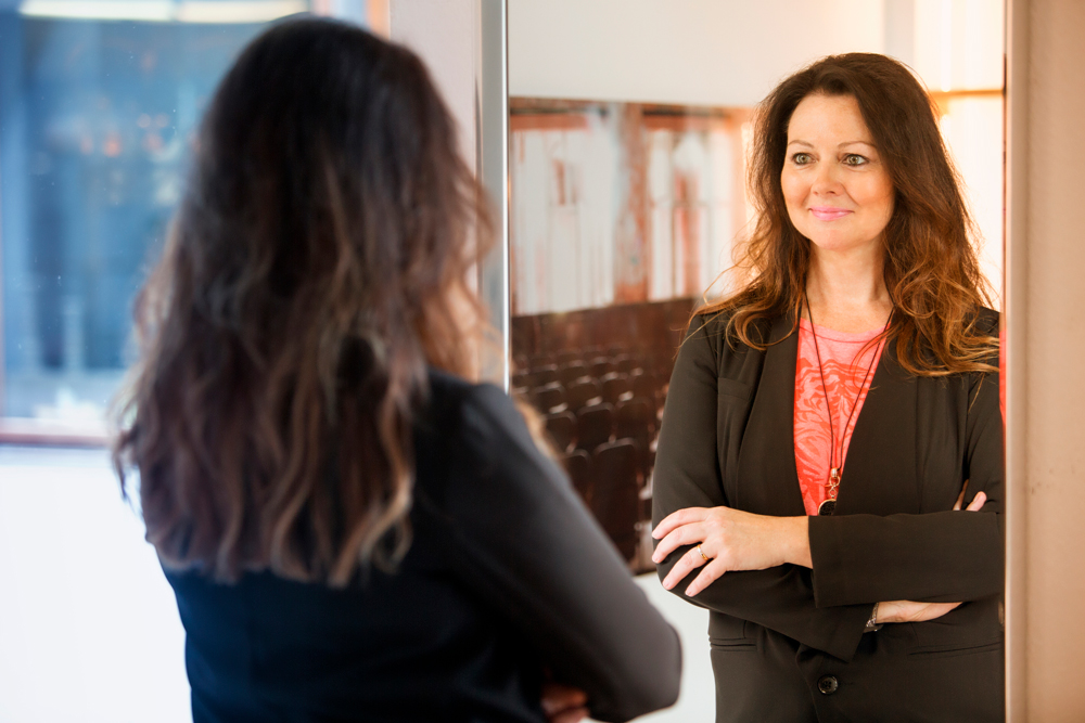 woman looking at her reflection in the mirror - how to say no to negative self talk