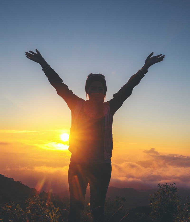 woman standing at the top of a mountain at sunset